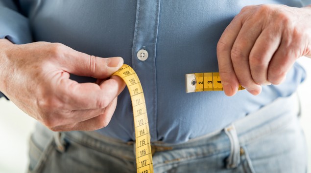Ein übergewichtiger Mann legt ein Maßband um seinen Bauch.