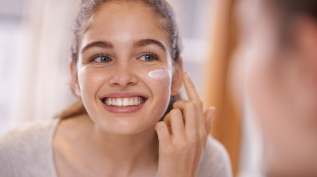 Eine junge Frau schmiert sich Creme ins Gesicht