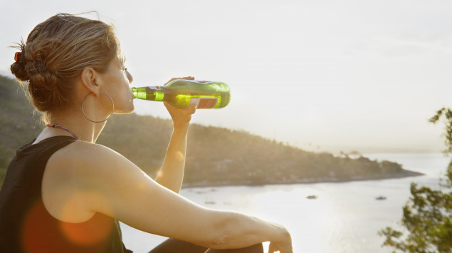 Eine Frau sitzt am Wasser und trinkt ein Bier.