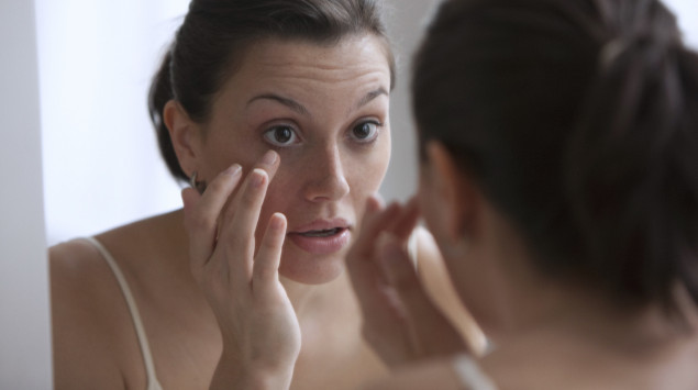 Eine Frau mit endokriner Orbitopathie untersucht ihre Augen im Spiegel.