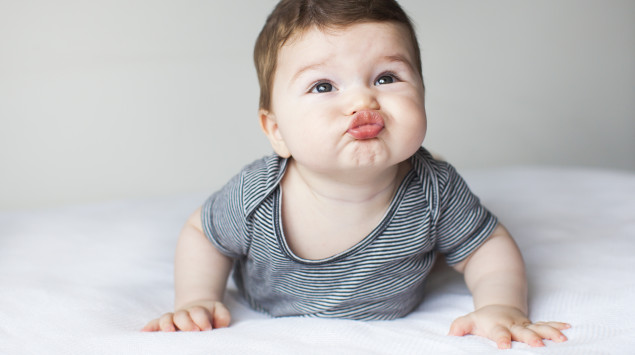 Ein Baby liegt auf dem Bauch, stützt sich ab und zieht eine Schnute