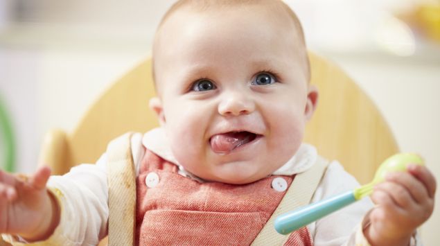 Ein fröhliches Baby hält einen Löffel.