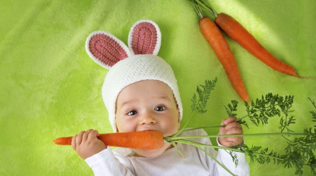 Ein Baby im Hasenkostüm knabbert an Möhren.