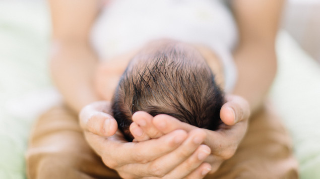 Eine Frau hält den Kopf eines Neugeborenen in den Händen. Hydrocephalus bei Kindern hängt häufig mit Spina bifida zusammen