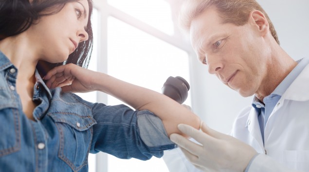 Ein Hautarzt untersucht eine junge Frau auf Hautkrebs.