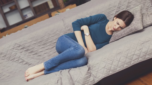 Durchfall: Eine Frau liegt mit Bauchschmerzen auf der Couch.