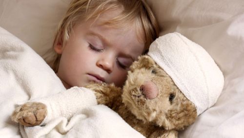 Das Bild zeigt ein krankes Kind im Bett mit einem Teddybären.