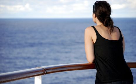 Eine Frau lehnt an der Reling und blickt aufs Meer.