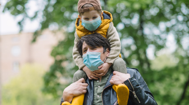 Ein Vater hat seinen Sohn auf den Schultern, beide tragen eine Maske.