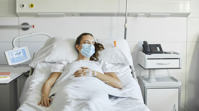 Eine junge Frau mit Mundschutz liegt im Krankenhausbett
