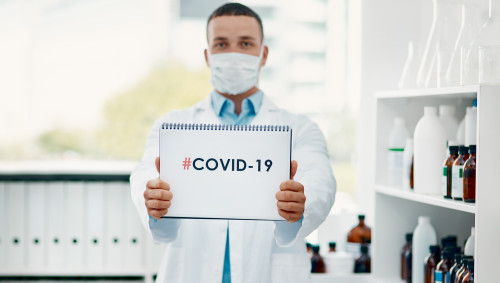 Ein Arzt mit Mundschutz hält einen Block hoch, auf dem Covid-19 steht