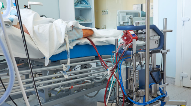 Man sieht einen Intensivpatienten im Bett, daneben eine ECMO