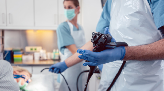 Eine Frau liegt auf einem OP-Tisch, ein Arzt hält ein Endoskop, eine Krankenschwester steht daneben