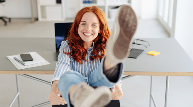 Eine Frau sitzt auf ihrem Bürostuhl im Büro und lacht.