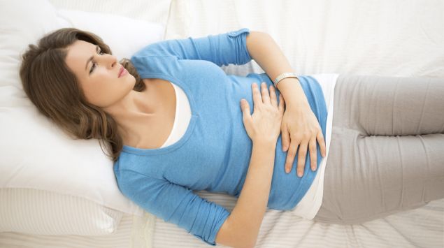 Eine Frau liegt mit Bauchschmerzen auf dem Bett.