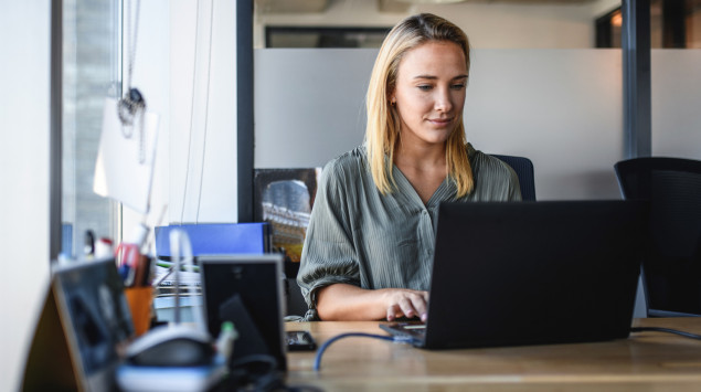 Eine Frau sitzt an ihrem Arbeitsplatz vor einem Laptop: Langes Sitzen kann zum Gesundheitsproblem werden.
