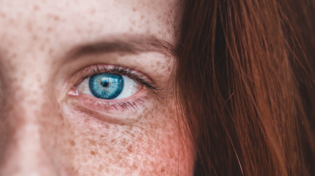 Das Foto zeigt den Gesichtsausschnitt einer Frau mit blauen Augen, roten Haaren und Sommersprossen.