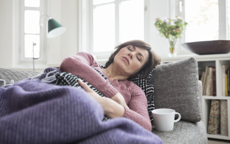 Was hilft gegen Durchfall? Eine Frau liegt auf dem Sofa und hält sich den Bauch.