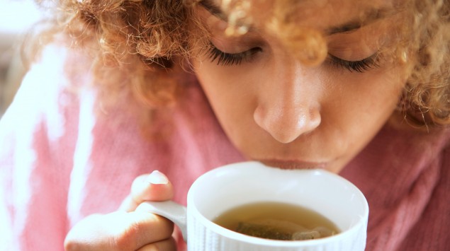 Eine junge Frau nippt an einer Tasse Tee.