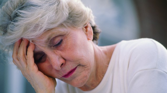 Eine ältere Frau stützt müde den Kopf auf.