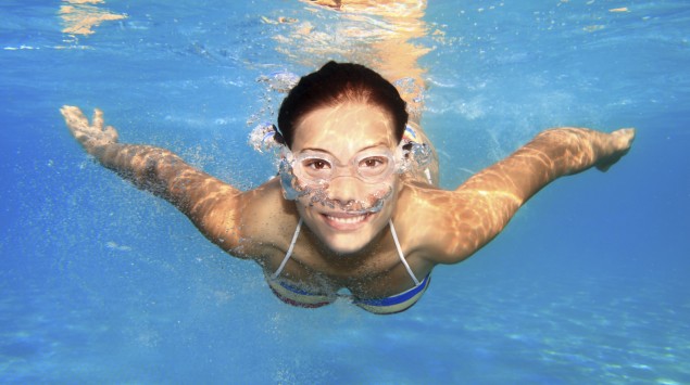 Eine junge Frau mit Schwimmbrille schwimmt unter Wasser.