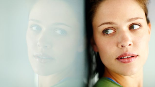 Das Gesicht einer jungen Frau wird von einer Scheibe reflektiert.
