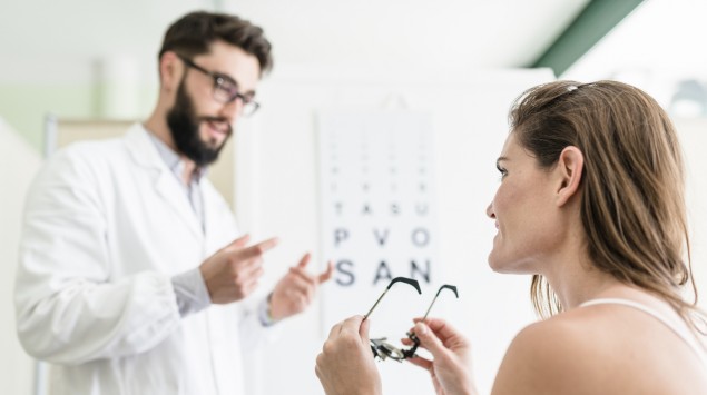 Eine Frau hält eine Brille in den Händen, während sie mit einem Augenarzt spricht.