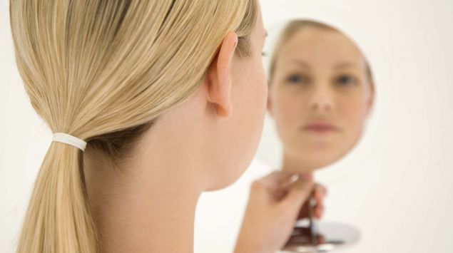 Eine Frau betrachtet sich in einem Spiegel.