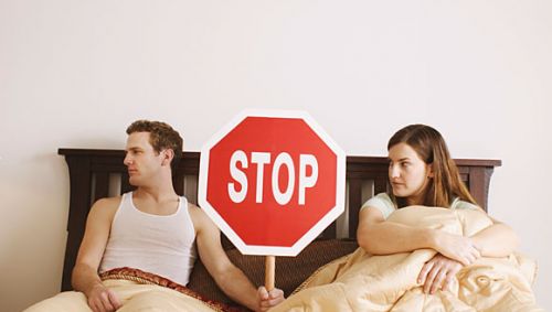 Ein Paar im Bett, in der Mitte ein Stopp-Schild.