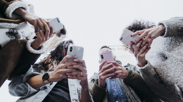 Mehrere junge Leute stehen zusammen und beschäftigen sich mit ihren Smartphones.