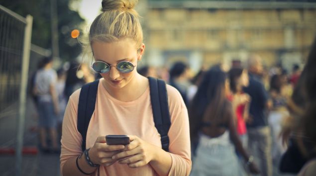 Das Bild zeigt eine junge Frau, die auf ihr Handy starrt.