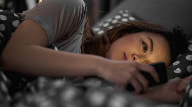 Eine junge Frau liegt im Bett und schaut auf ihr Smartphone.