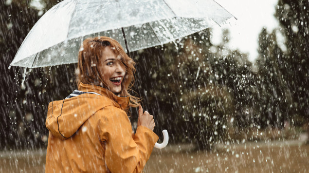 Eine Frau geht bei regnerischem Wetter mit Schirm spazieren und lacht