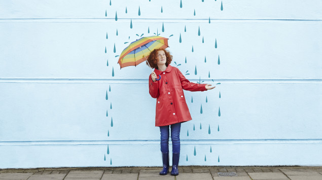 Eine Frau mit Schirm steht vor einer Wand, auf der Regen gemalt ist