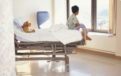 Das Bild zeigt einen Jungen, der allein auf einem Krankenhausbett sitzt.