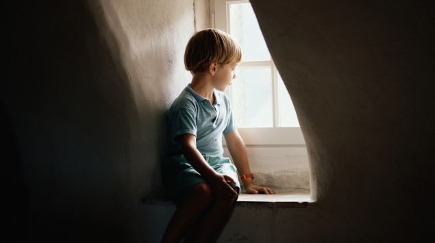 Das Bild zeigt einen kleinen Jungen, der allein am Fenster sitzt.