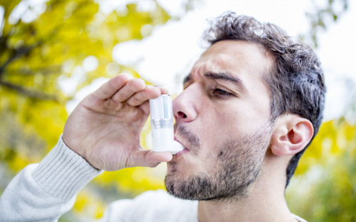 Ein junger Mann inhaliert sein Asthmaspray.