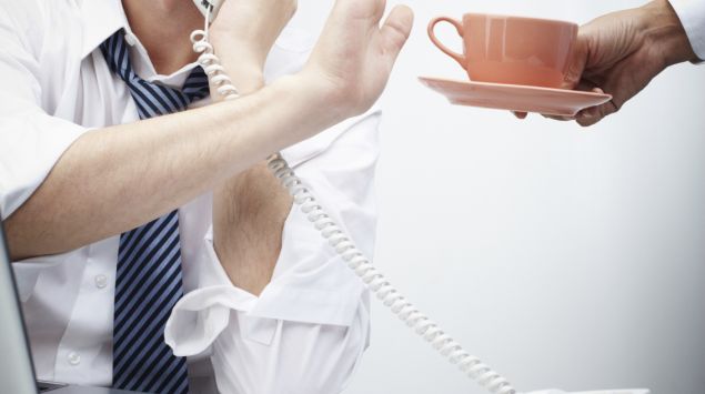 Ein telefonierender Mann lehnt mit einer Handbewegung eine Tasse Kaffee ab.