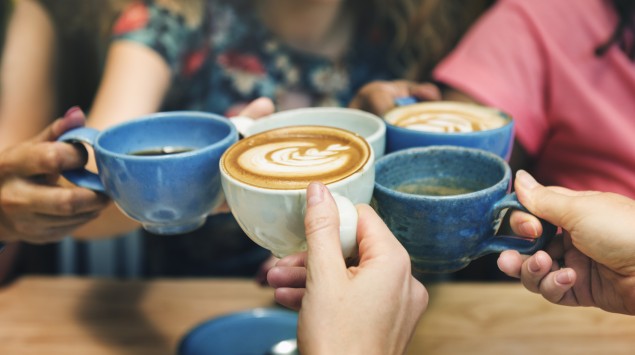 Fünf Freundinnen stoßen mit Kaffee an.