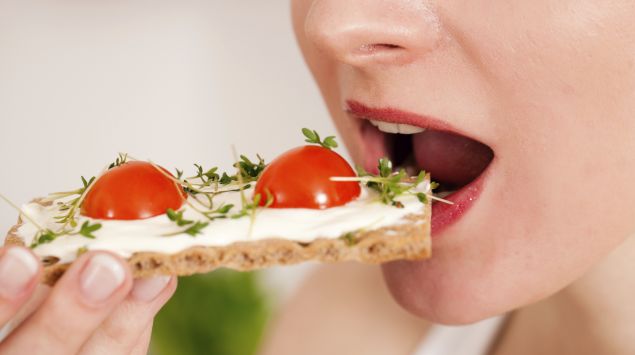 Frau isst Knäckebrot mit Tomaten und Kresse