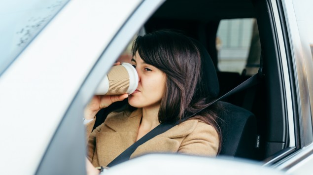 Eine Frau am Steuer eines Autos trinkt Kaffee aus einem Becher.