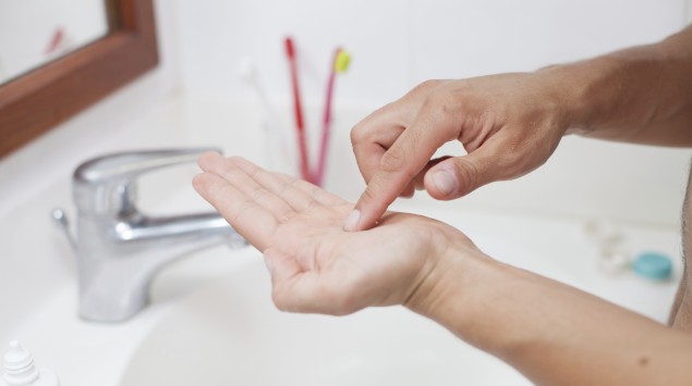 Zu sehen sind die Hände eines Mannes, der gerade über einem Badezimmerwaschbecken eine Kontaktlinse reinigt.