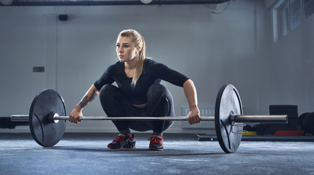 Eine Frau im Fitnessstudio mit einer Langhantel.