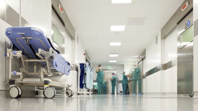 Das Bild zeigt einen Krankenhausflur mit einem Bett und Personal.