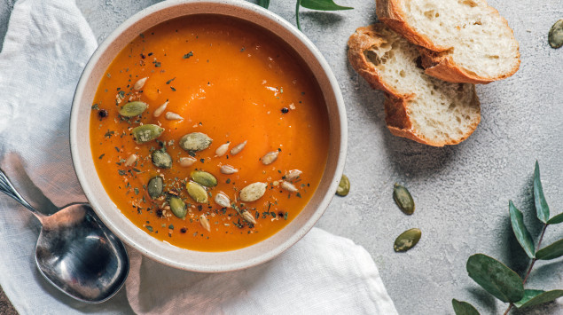 Eine Schüssel mit Kürbissuppe, Kürbiskernen und zwei Scheiben Baguette.