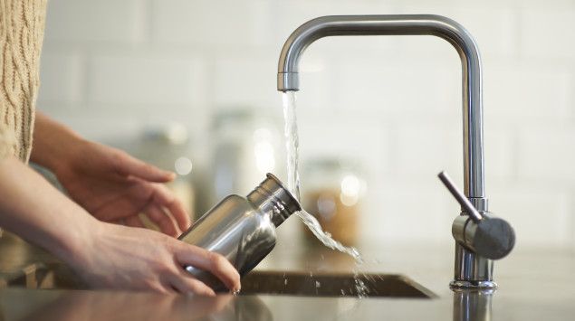 Eine Person füllt eine Trinkflasche am Wasserhahn mit Trinkwasser.