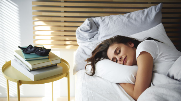 Eine Frau liegt im Bett und schläft, neben ihr ein Stapel Bücher.