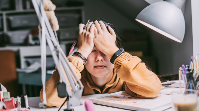 Eine Frau sitzt erschöpft und verzweifelt über Büchern