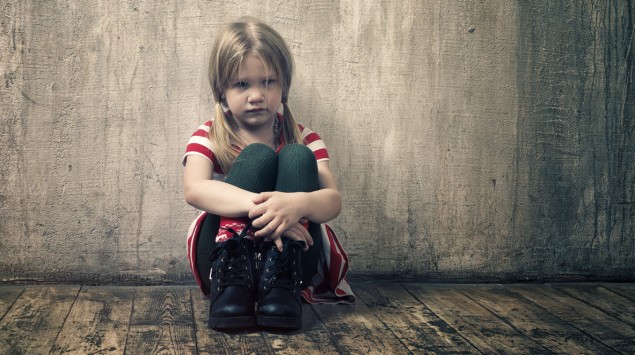 Ein kleines Mädchen sitzt an einer Wand.