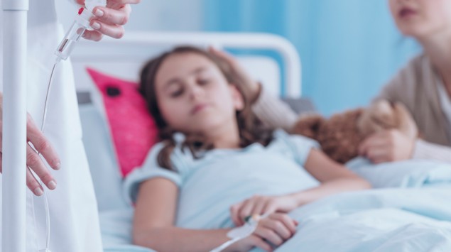 Ein Mädchen liegt in einem Krankenhausbett und hängt an einem Tropf.